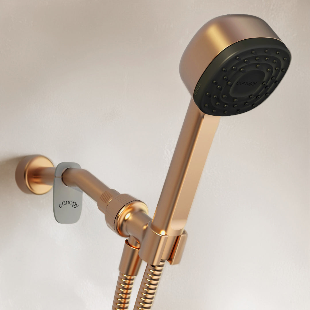 A sleek, modern shower head with a brass finish, reminiscent of the beauty and skincare industry's elegance. Mounted on the wall, it features a flexible hose and simple design. The brand name canopy is visible on both the head and mount, ensuring a luxurious touch akin to a high-end diffuser.