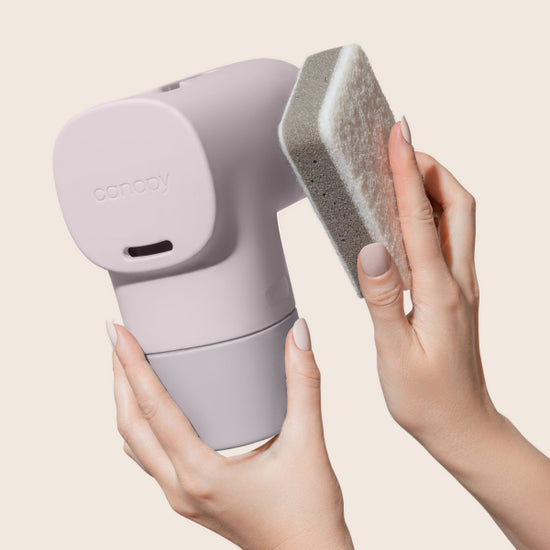 One hand holding the Bath Tub Filter in Lavender and the other wiping the device using a sponge