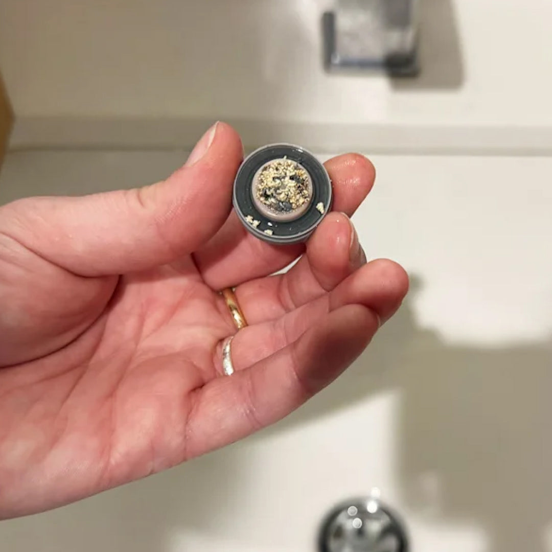 Hand holding a dirty bathroom faucet aerator, showcasing the various contaminants that are lurking in your tap water