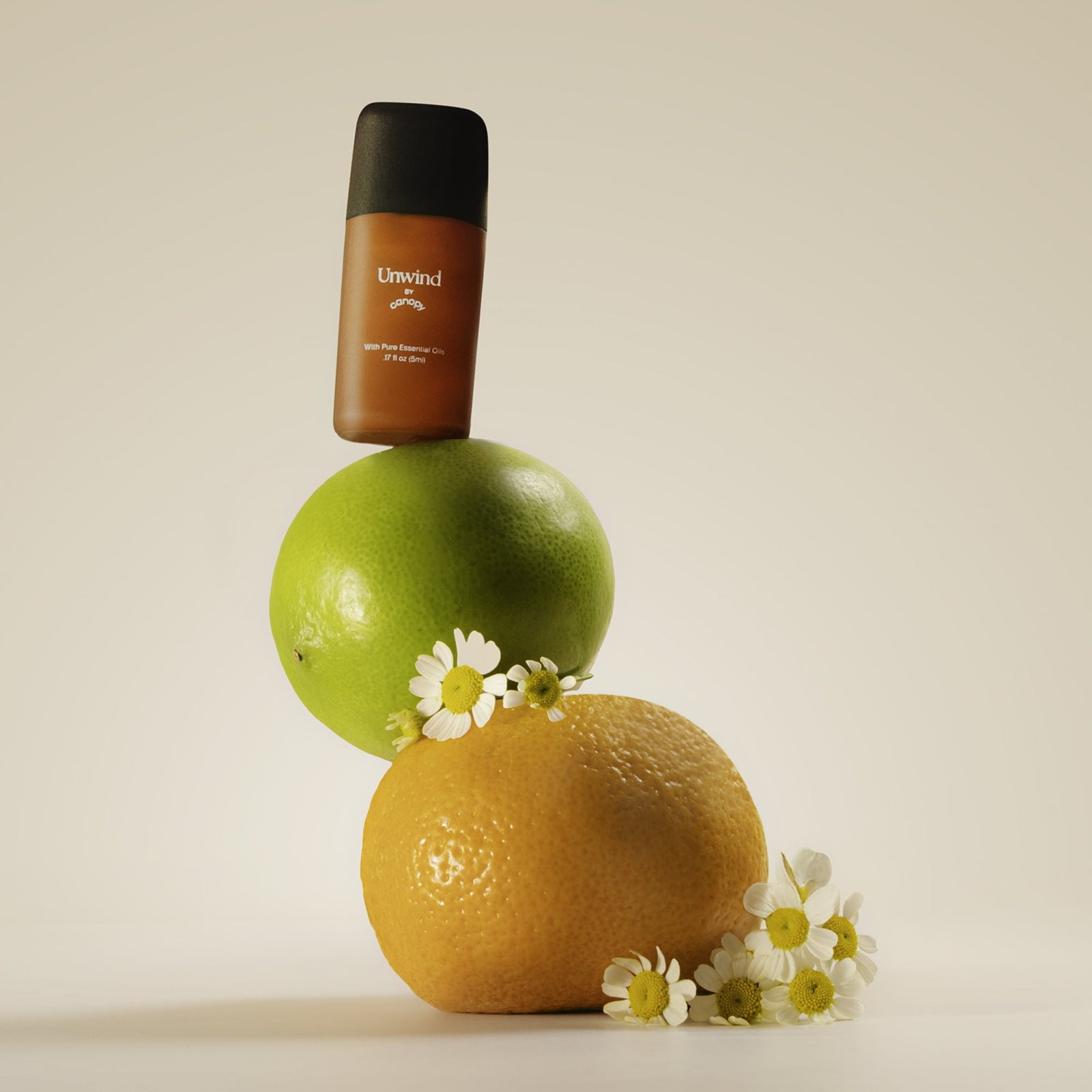 Unwind Aroma | Lifestyle, Aroma bottle of Unwind balanced on a green lime and orange with flowers on a beige background