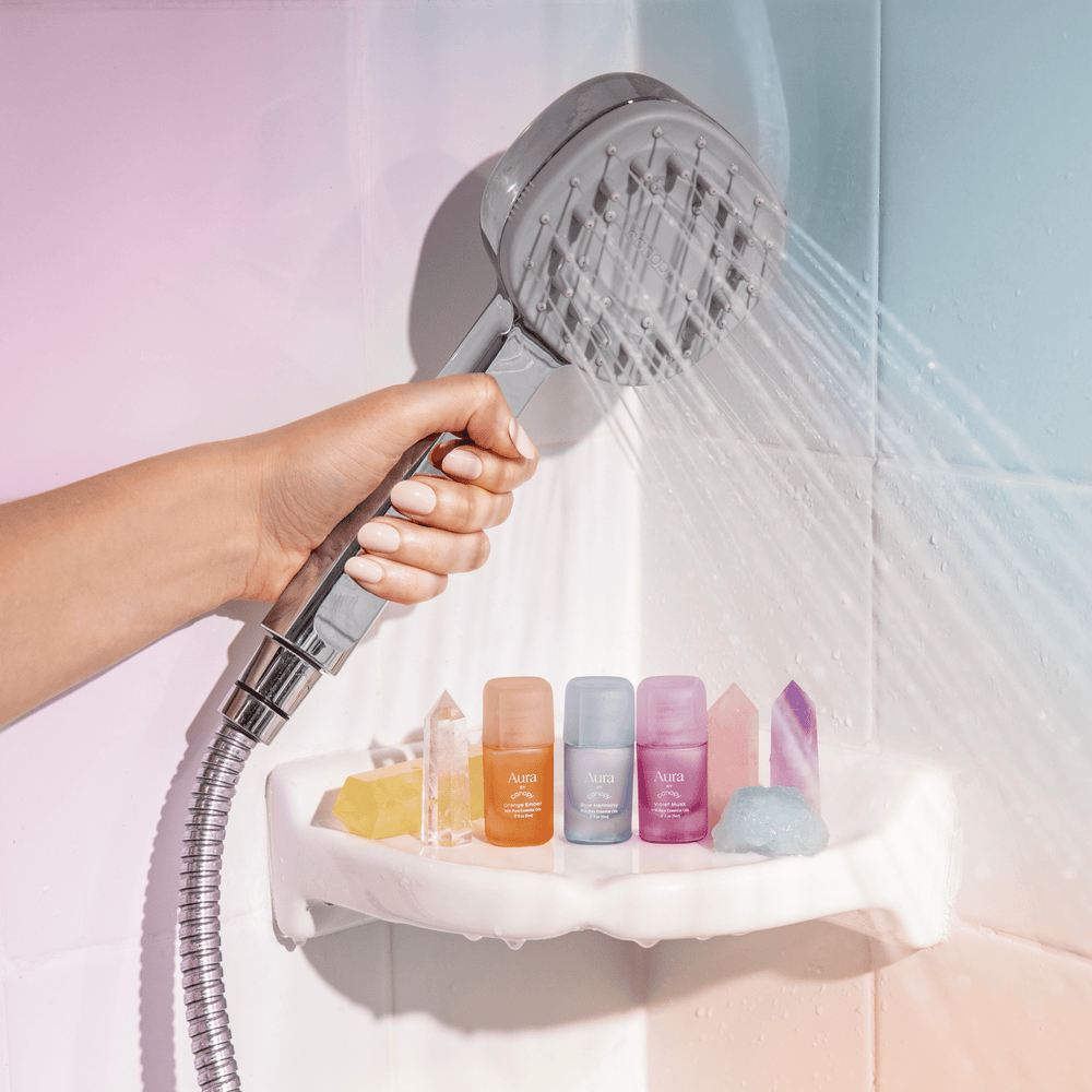 Aura Aroma Kit | Lifestyle, Aroma Kit paired with the Handheld Filtered Showerhead in Polished Chrome with water coming out of the Showerhead on a beautiful gradient background of pink, blue, and orange