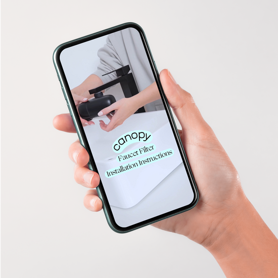 Hand holding phone on a grey background showcasing the Faucet Filter ste-by-step installation video