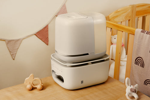 Nursery All-in-One Humidifier & Purifier on wooden table next to crib with toys nearby
