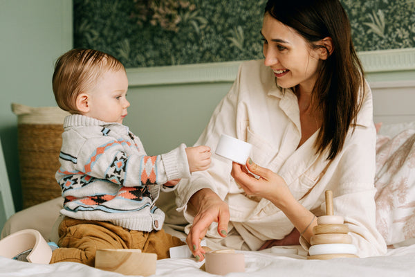 Mother and baby playing with wooden toys on bed