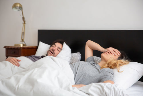 Woman struggling to sleep while male partner is snoring in bed
