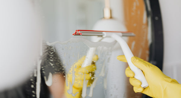 Cleaning glass surface in bathroom with squeegee