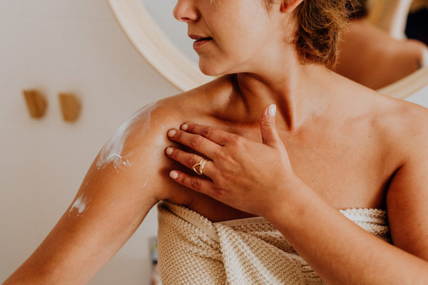 Woman in bathroom applying body lotion after shower