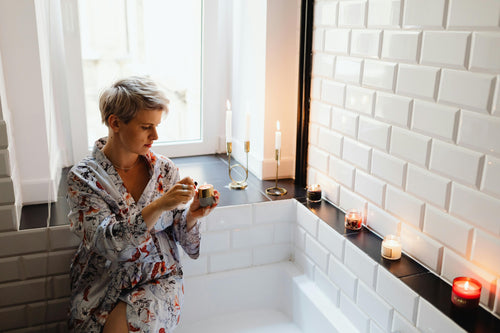 Woman in bathrobe lighting candles around black and white bathtub