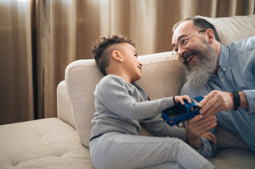 Grandfather and grandson playing with toy truck on sofa