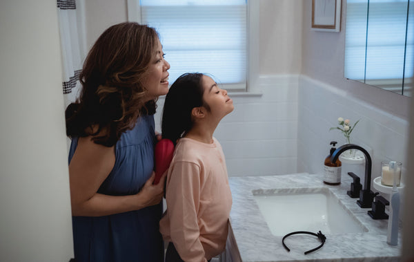 Woman brushing daughter's hair in bathroom