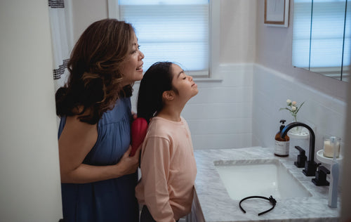 Woman brushing daughter's hair in bathroom