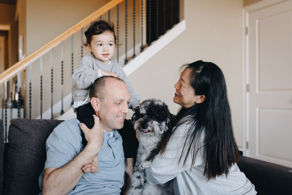 Parents, toddler, and pet dog together on couch in downstairs room of home