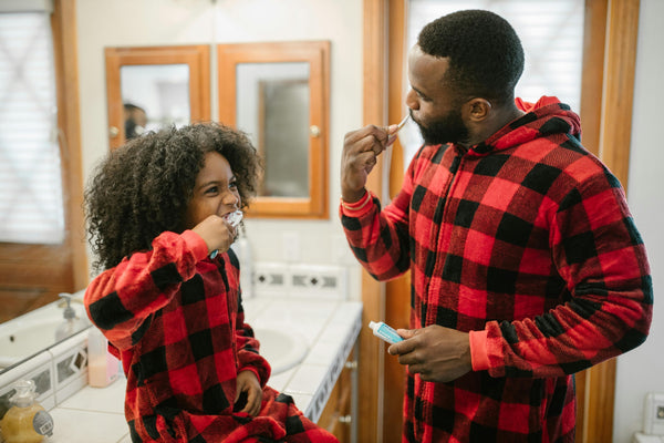 Father and child dressed in matching red plaid pajamas brushing teeth