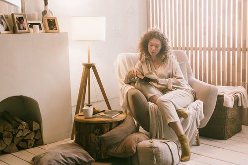 Woman reading next to fireplace with logs