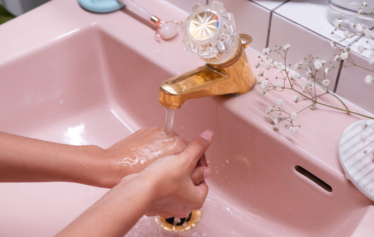 Woman washing hands in pink vintage-style sink with brass faucet fixture