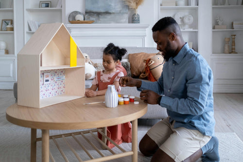 Father and daughter painting dollhouse together in white living room