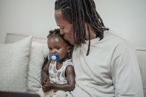 Father sitting on white bed kissing baby's head