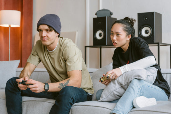 Young man and woman playing games on living room sofa with large speakers in the background