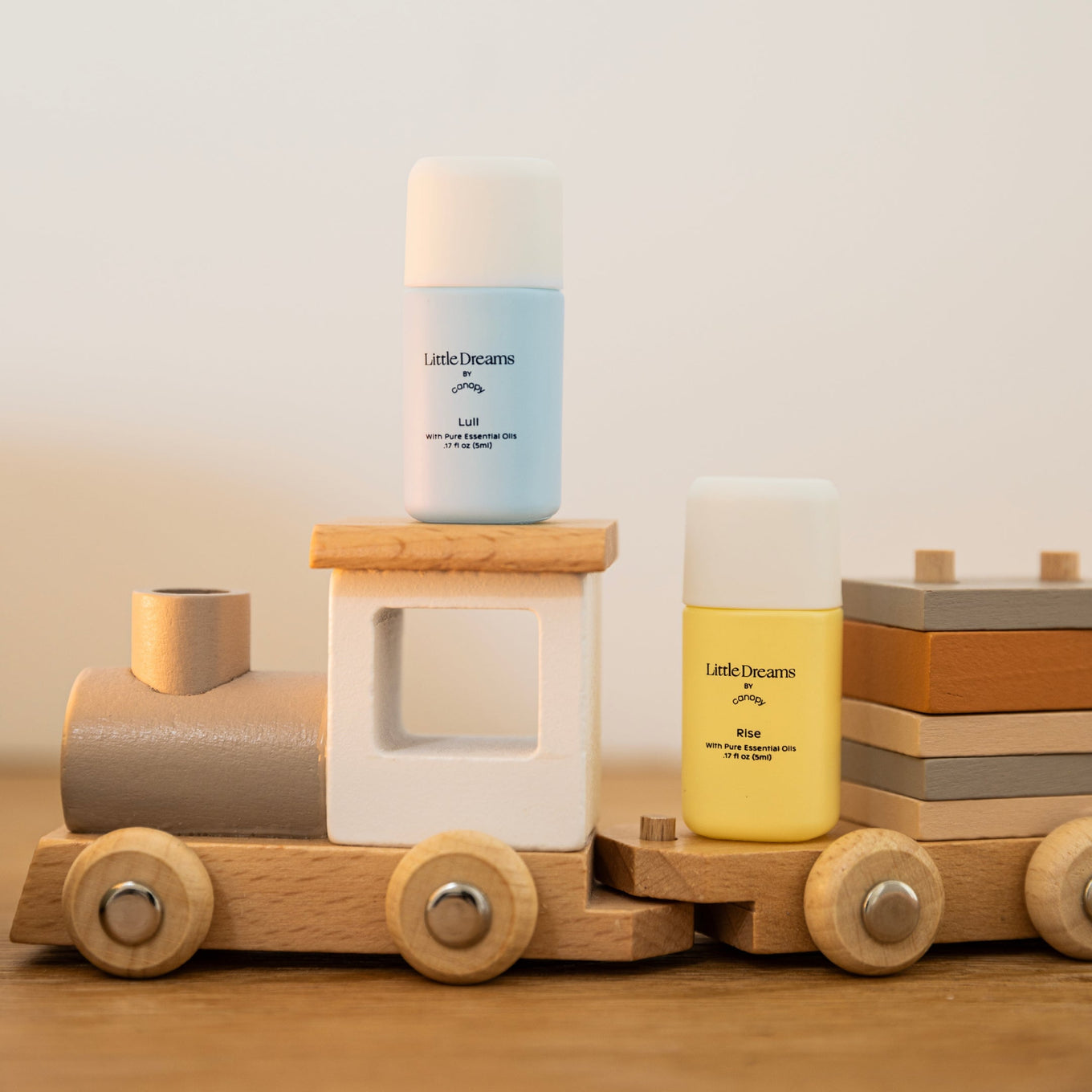 Little Dreams Aroma Kit displayed on a charming wooden toy train set, featuring light blue and yellow aromatic bottles arranged on wooden train cars, showcasing a playful and nursery-friendly design by Canopy