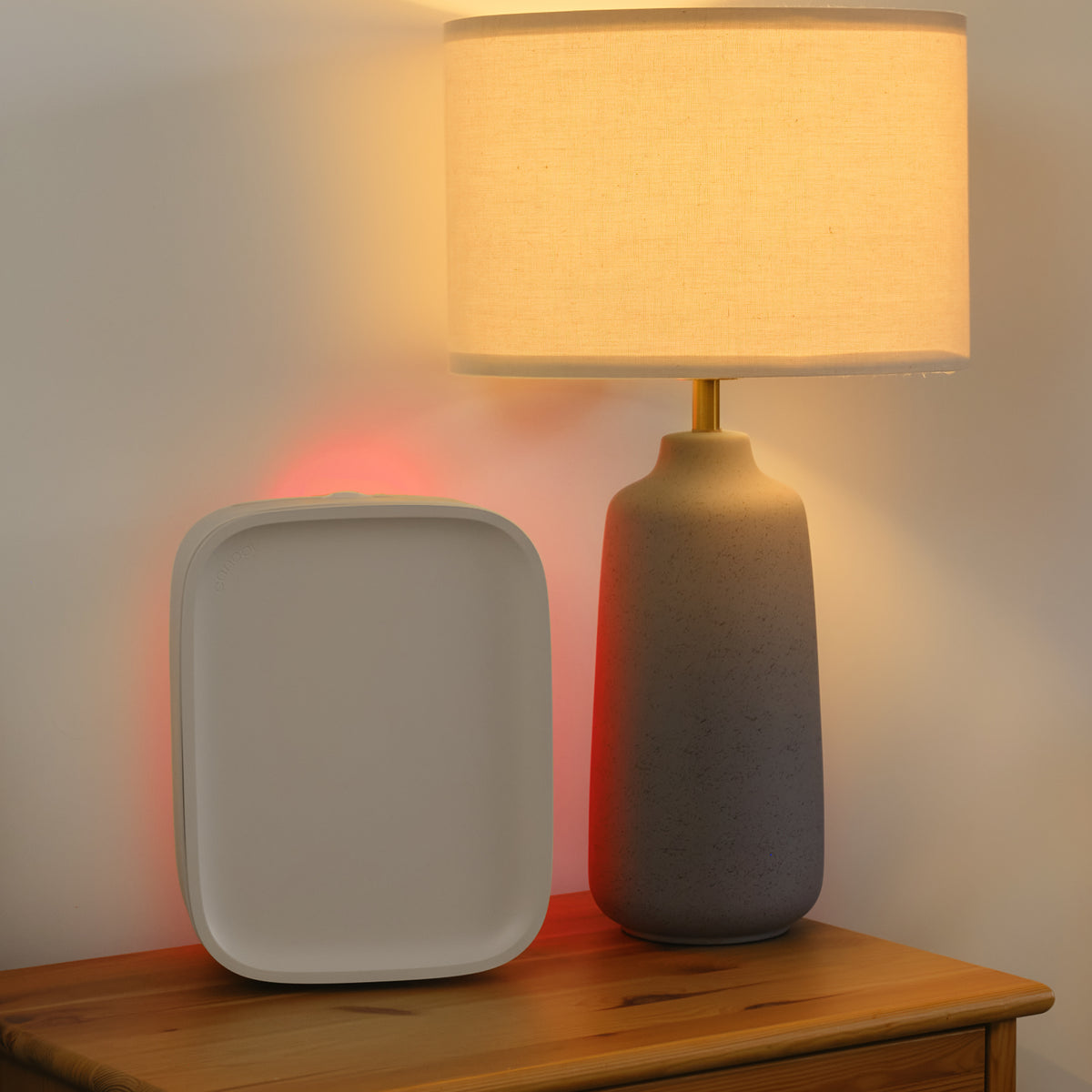 Table lamp with a beige shade and gray base next to an air purifier with a red glow
