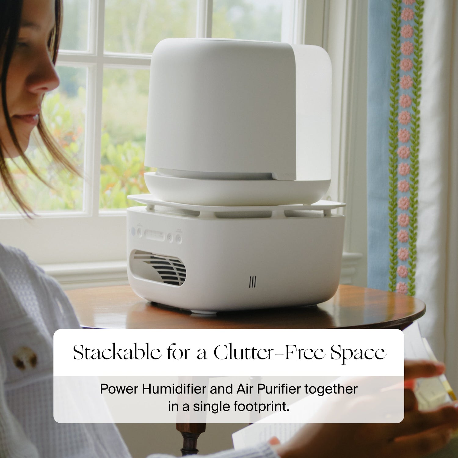Bedside Air Purifier | Lifestyle, stackable for a clutter-free space, power humidifier and air purifier together in a single footprint. Photo of White humidifier and air purifier on a table with a person in the background.