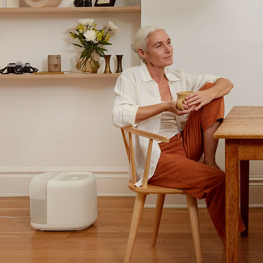 Modern white Large Room Humidifier Device Filter & Aroma unit shown in cozy home setting with wooden furniture, featuring sleek design on hardwood floor. Creates comfortable living space atmosphere with aromatherapy capabilities by Canopy.