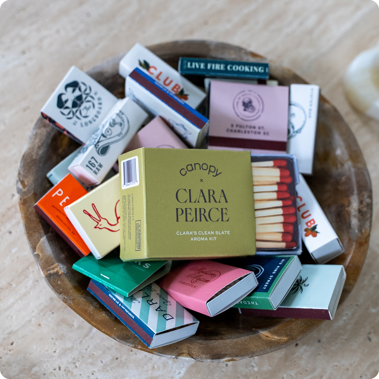 Clean Slate Aroma Kit | Lifestyle, Clara Peirce Aroma Kit box designed as a match box laying with various matchboxes in a wooden bowl on a light wooden surface.