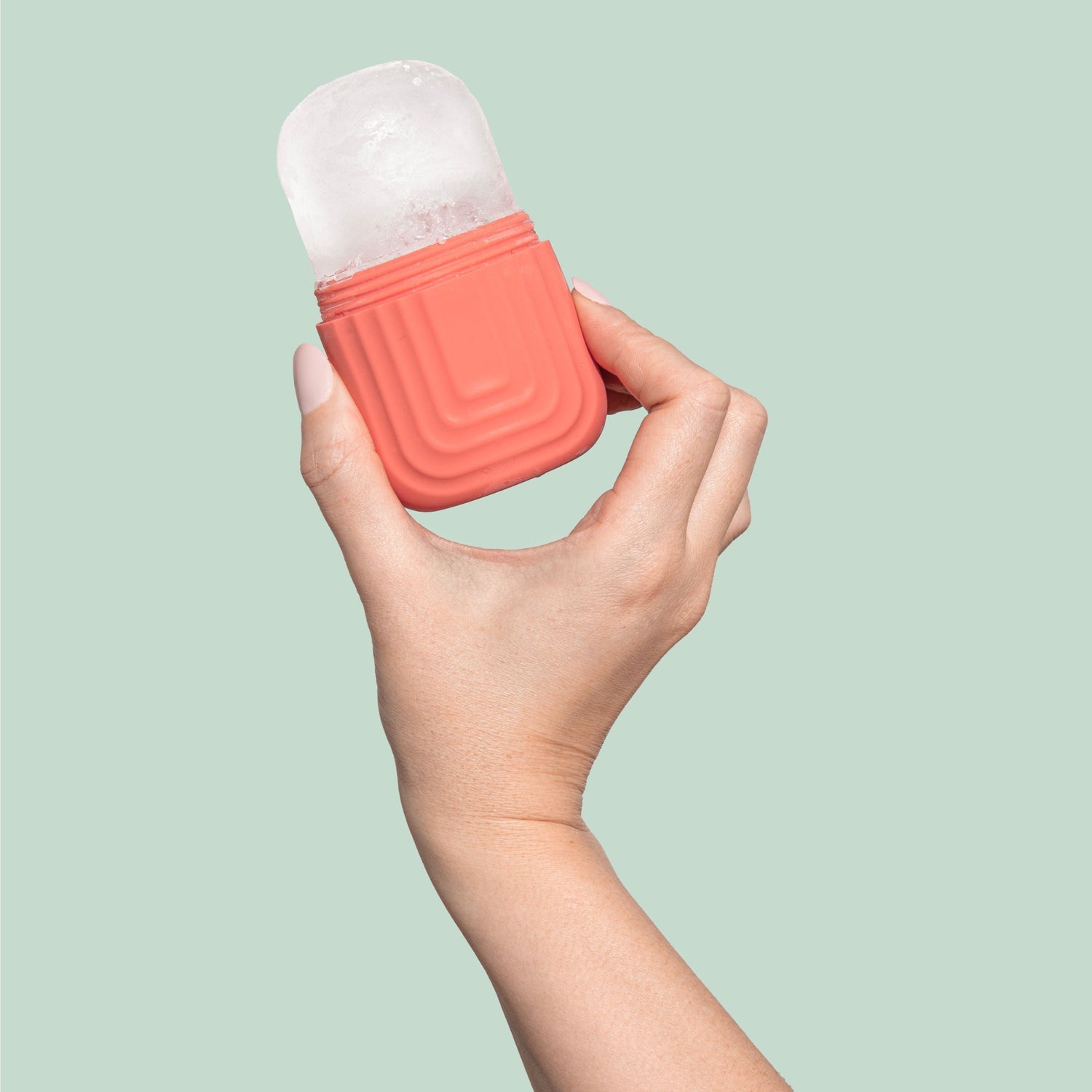 Ice Roller | Lifestyle, hand holding coral ice roller with ice inside 