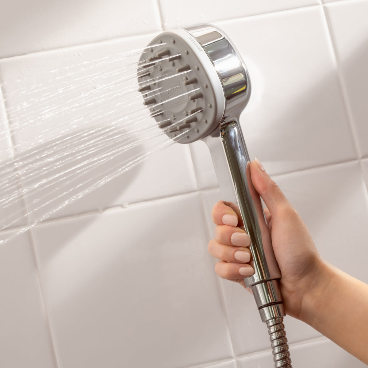 Handheld shower head spraying water against white tiled background