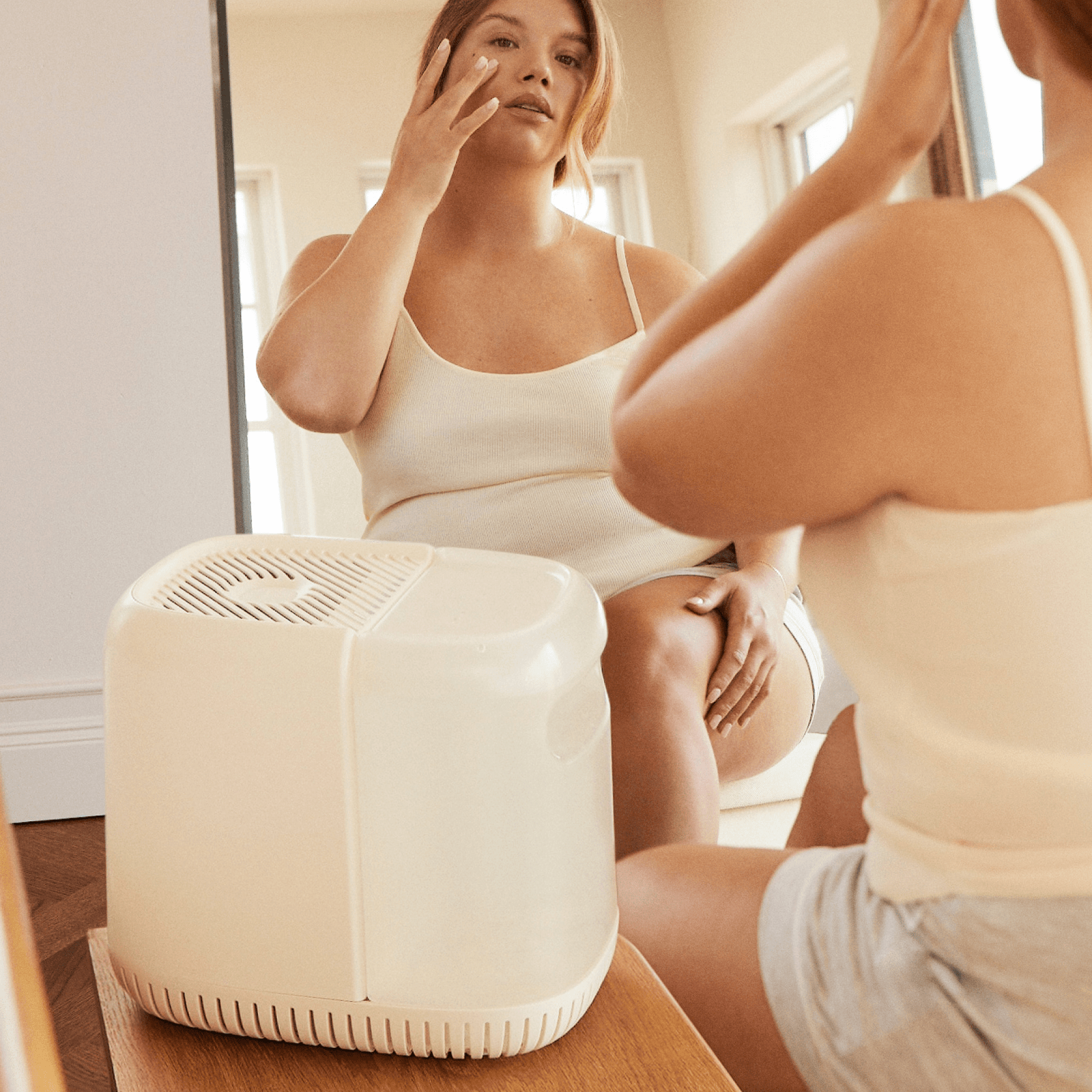 Bedside Humidifier | Lifestyle, Woman sitting next to a Canopy Bedside Humidifier and admiring her glowing skin in the mirror