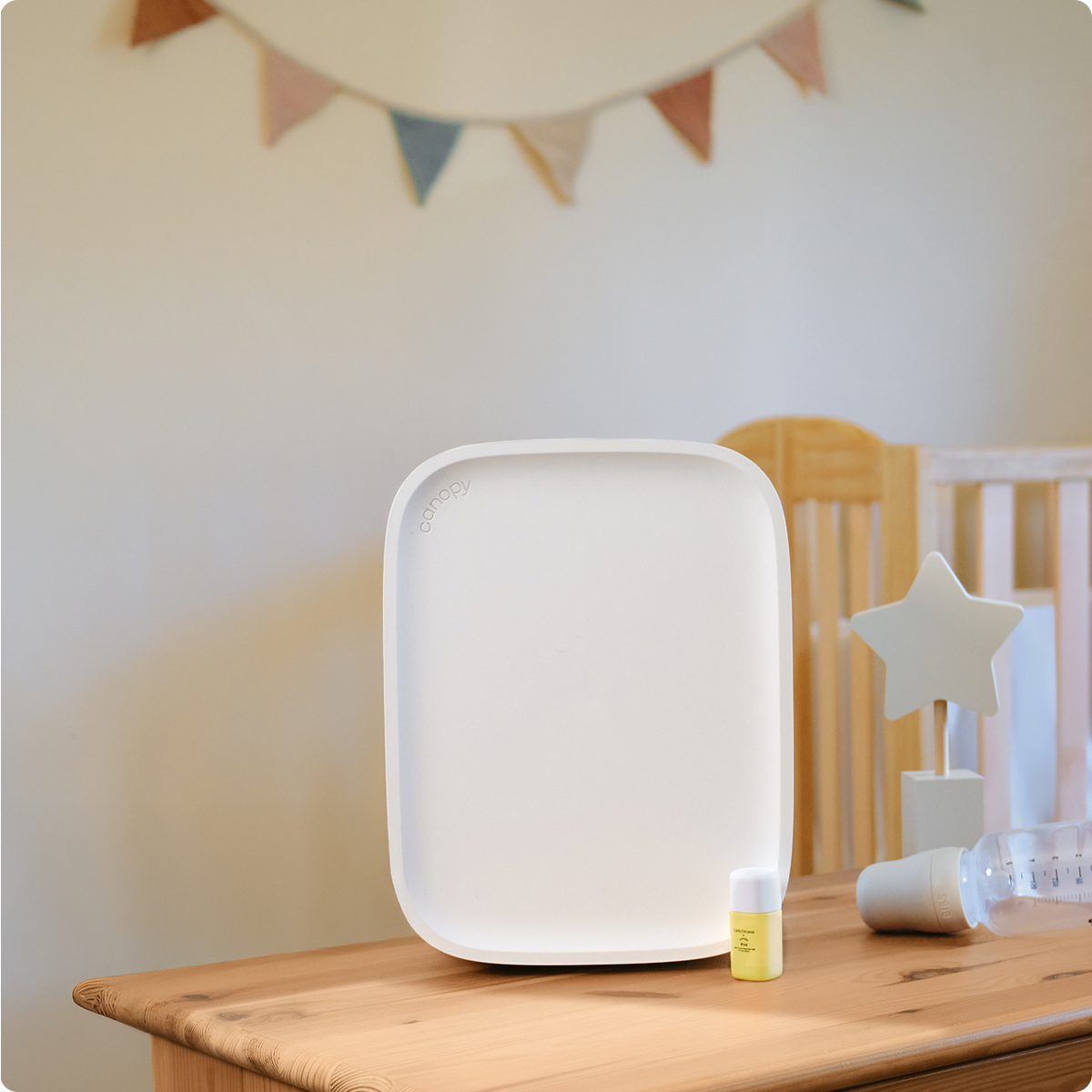 White air purifier on a wooden surface with a crib and decorative flags in the background